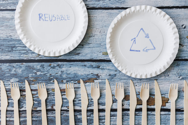 浅蓝色木制背景上的环保餐具平面组合。牛皮纸盘子和木制餐具。可回收的纸制品，零浪费的理念。有选择性的重点图片下载