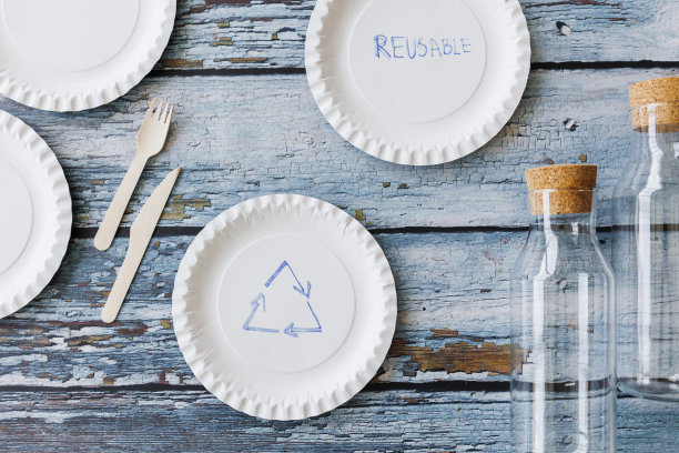 浅蓝色木制背景上的环保餐具平面组合。牛皮纸盘子和木制餐具。可回收的纸制品，零浪费的理念。有选择性的重点图片下载