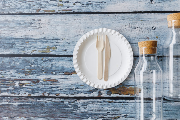 浅蓝色木制背景上的环保餐具平面组合。牛皮纸盘子和木制餐具。可回收的纸制品，零浪费的理念。有选择性的重点图片下载