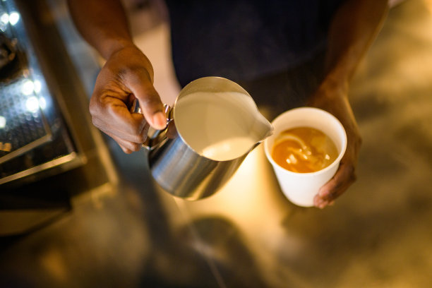 咖啡师准备将起泡牛奶倒入咖啡一次性纸杯中图片下载