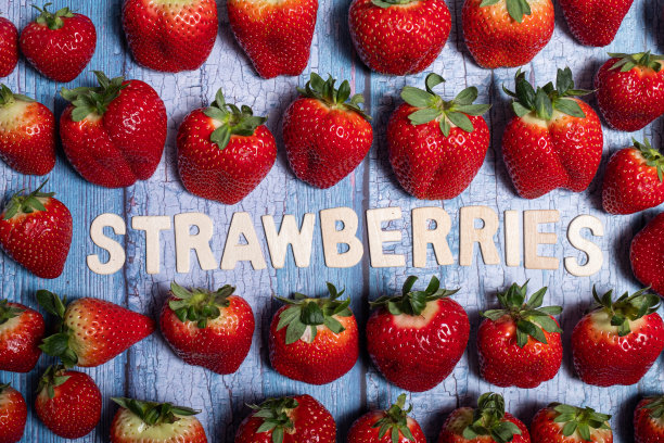 红色美味的草莓与草莓的水果写在蓝色的木头表面图片下载
