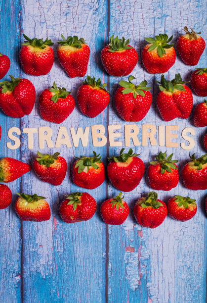 红色美味的草莓与草莓的水果写在蓝色的木头表面图片下载