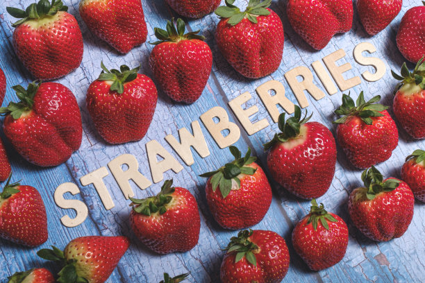 红色美味的草莓与草莓的水果写在蓝色的木头表面图片下载