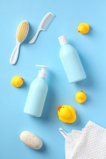 婴儿洗发香波和沐浴露与沐浴配件在蓝色的背景。平铺，俯视图洗发水瓶，沐浴露，黄橡皮鸭，毛巾，肥皂，梳子。图片下载