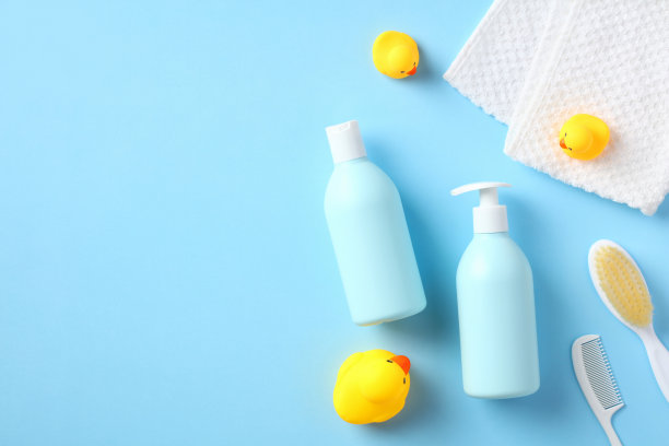 平铺，俯视图婴儿洗发水瓶，沐浴露，毛巾，梳子，刷子，蓝色背景上的黄色橡皮鸭。婴儿洗澡的概念。图片下载