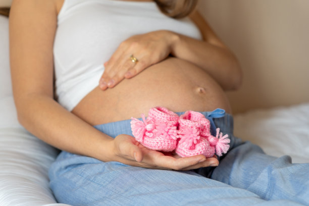 怀孕宝宝鞋子。幸福的孕妇抱着粉红色的婴儿鞋。小孩的鞋。怀孕的概念，母性，对婴儿的期望。图片下载