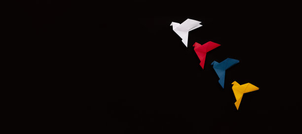 横幅上的三只白纸折纸鸽子白、红、蓝、黄在黑色的背景上斜着飞起来图片下载