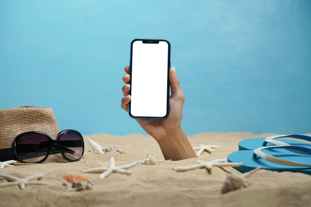 手拿着白色的智能手机穿过沙滩。在智能手机上创建媒体。图片下载