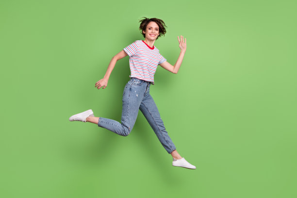 全长身体大小侧面看法漂亮开朗的女孩跳跑挥舞hi孤立在绿色粉彩背景图片下载