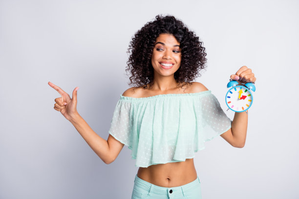 照片肖像狡猾的女孩指着空白的手指在一只手拿着闹钟孤立在白色背景图片下载