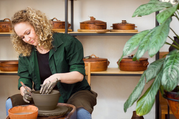 陶艺车间里的金发卷毛女人。陶轮上的陶碗。陶瓷类工作室图片下载