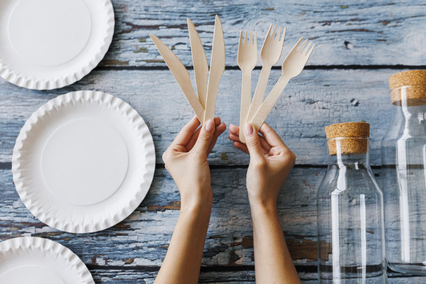 浅蓝色木制背景上的环保餐具平面组合。牛皮纸盘子和木制餐具。可回收的纸制品，零浪费的理念。有选择性的重点图片下载