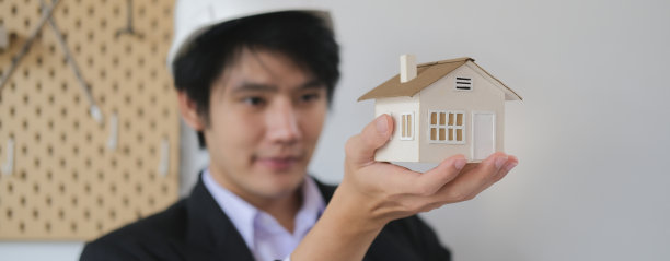 有思想的男建筑师戴着安全帽，拿着并看着房子模型。图片下载