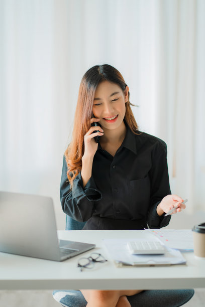 亚洲女商人，手持智能手机，用笔、笔记本电脑和计算器分析报告。在工作站会计网上营销概念电子商务垂直形象图片下载