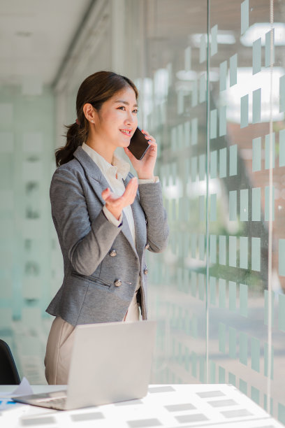 亚洲女商人，手持智能手机，用笔、笔记本电脑和计算器分析报告。在工作站会计网上营销概念电子商务垂直形象图片下载