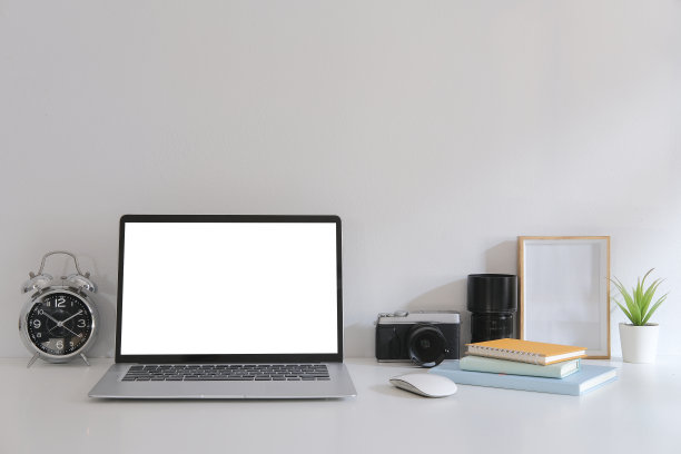 白色的桌子上放着笔记本电脑、相机、书和相框。图片下载