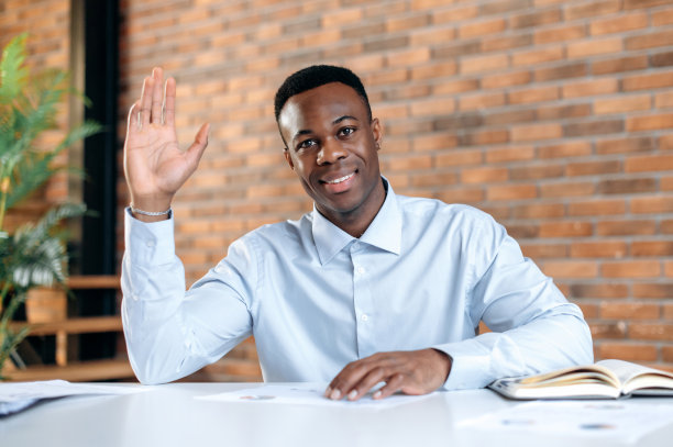 网络摄像头大头特写，友好，聪明的年轻黑人男性，年长经理，财务顾问，坐在办公室的桌子上，与同事交谈，参与视频通话，挥手，微笑图片下载