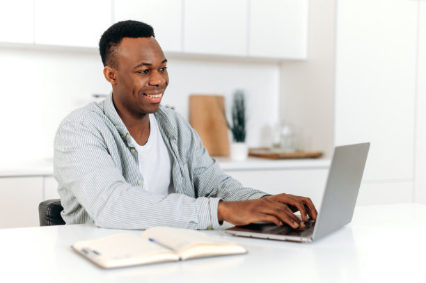 有吸引力的积极的非洲裔美国人，自由职业者，设计师，IT专家，在家用笔记本电脑工作，制定策略，分析，与客户或同事通信，浏览互联网，微笑图片下载