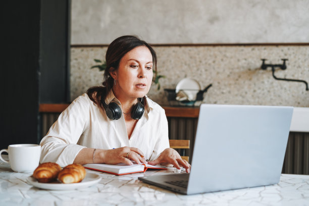 成年微笑的黑发女人戴着耳机在家里打开笔记本电脑做笔记图片下载