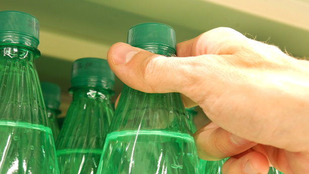 商店货架上许多装着碳酸水的绿色塑料瓶的特写，一个男性买家拿着一个图片下载