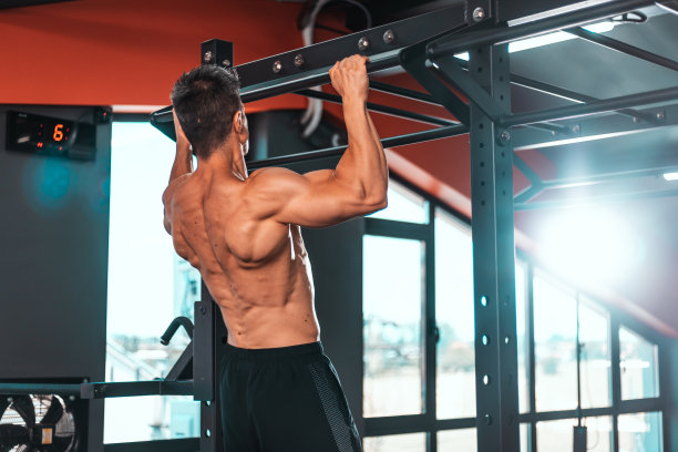 肌肉发达的运动员在健身房做单杠引体向上的背影。运动教练在健身房锻炼锻炼。身材健美，体格健壮，上身赤裸，穿着黑色短裤。图片下载