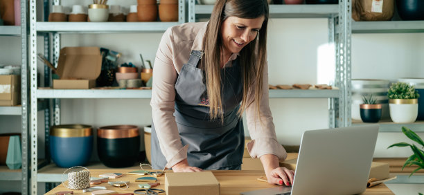 微笑的女人在笔记本电脑上阅读网上订单，并准备在她的商店交付的圣诞粘土饰品图片下载