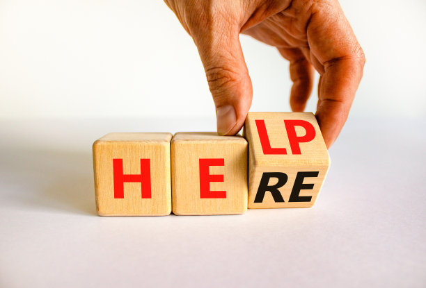 帮助在这里是支持符号。商人将木制立方体，将“帮助”这个概念改为“这里”。漂亮的白色表格白色背景，复制空间。业务支持帮助是这里的概念。图片下载