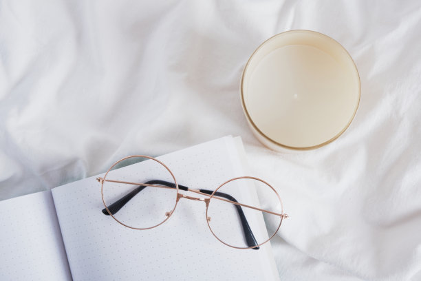 眼镜，香薰蜡烛和开在白色皱巴巴的布上的空白记事本图片下载