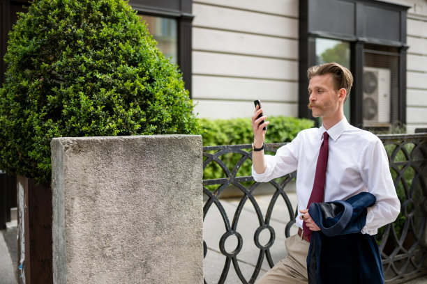 一个留着小胡子的潮男在城市里散步，一边用手机看短信，一边打电话，图片下载