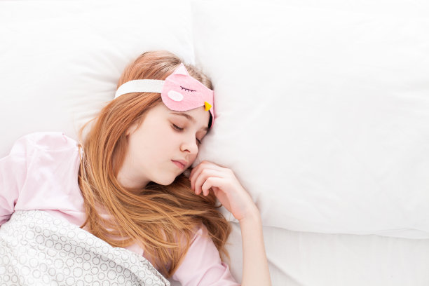 睡觉的女孩戴着有趣的眼罩躺在床上的毯子。图片下载