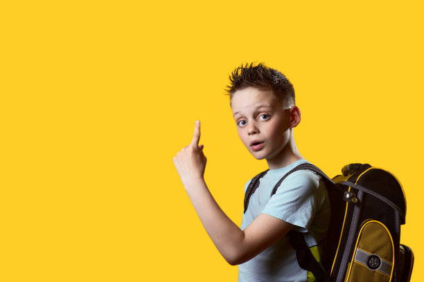 9月，一年级男生背着书包回到学校，黄色的背景是课本，秋的概念。图片下载