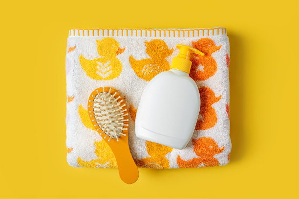 宝宝毛巾与可爱的鸭子和肥皂或洗发水瓶与梳子在黄色的背景。沐浴配件图片下载