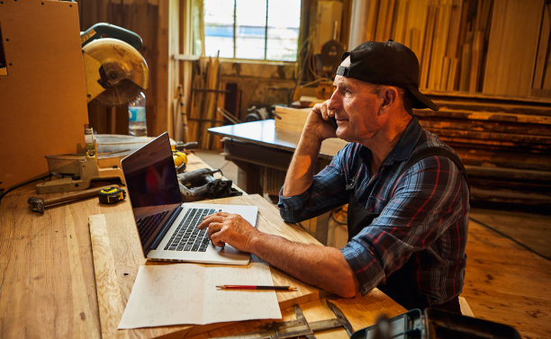 高级木匠在车间用电脑工作，与客户电话交流图片下载