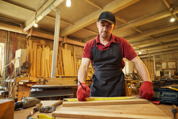 木匠在木工车间用木头工作，用铅笔在木板上做记号，测量尺寸，切割一块木头制作家具图片下载