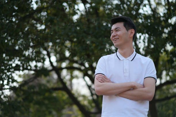 亚洲年轻人交叉手臂和微笑在绿色的公园图片下载