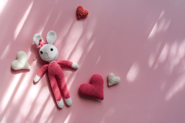 粉红色背景上编织的兔子和心形。可爱的装饰和配件的婴儿和儿童的房间。平铺，俯视图图片下载