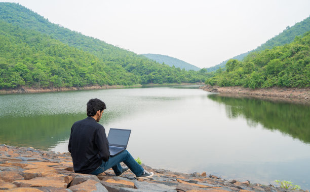 年轻人坐在大自然中，用笔记本电脑工作，工作和数字游牧民的概念。图片下载