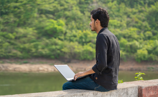 年轻人坐在大自然中，用笔记本电脑工作，工作和数字游牧民的概念。图片下载