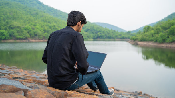 年轻人坐在大自然中，用笔记本电脑工作，工作和数字游牧民的概念。图片下载