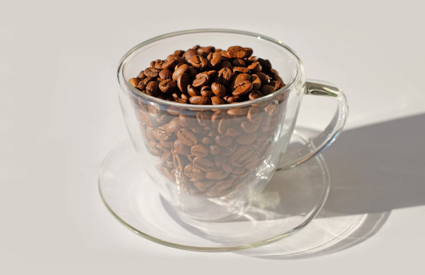 玻璃杯子充满了咖啡豆与阳光和阴影在白色背景特写图片下载