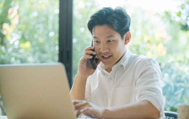 亚洲男性一边工作一边打电话，在家使用笔记本电脑图片下载