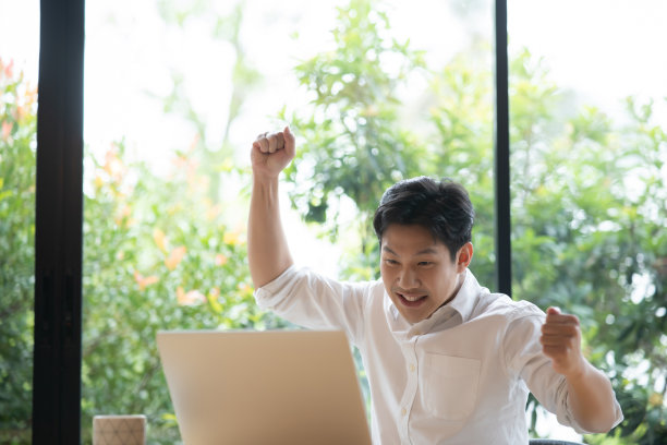 一名亚洲男子在家用笔记本电脑工作，庆祝成功。图片下载