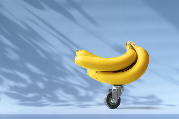 创意餐饮配送理念与文案空间。蓝色背景，购物车里的一串香蕉放在轮子上。图片下载