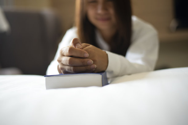 祈祷圣经的亚洲妇女。十几岁的亚洲妇女手拿圣经祈祷。为了信仰、灵性和宗教，双手合拢在圣经上祈祷。图片下载