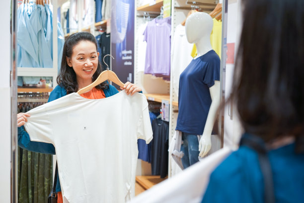 年轻的亚洲女人在布艺店的镜子前试尺寸的T恤。图片下载