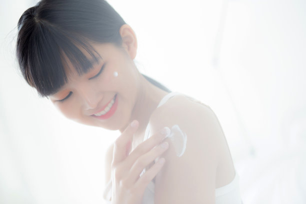 美丽的年轻亚洲女人快乐地应用面霜或乳液与保湿剂皮肤上的肩膀，美丽的亚洲女孩应用皮肤护理与化妆品的卫生和皱纹，皮肤护理的概念。图片下载