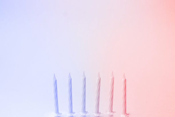 蓝色和红色背景的白色生日蜡烛。最小的生日派对概念，复制空间的愿望。准备好蛋糕。渐变色与光效果背景。图片下载
