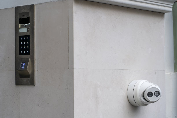闭路电视摄像头安全系统安装在墙上。墙上有视频监控摄像头，监控住宅入口。豪华住宅石灰石墙上的哑光金属对讲电话面板，白色数字按钮和指纹扫描仪图片下载