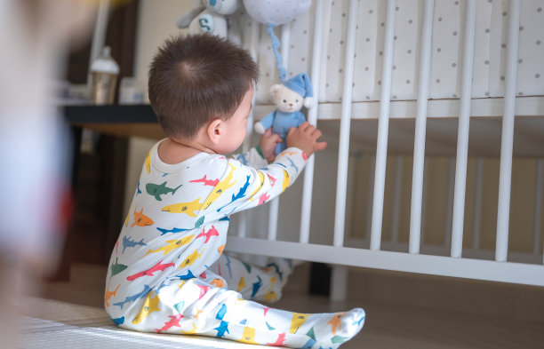 在卧室里玩挂在婴儿床上的拉动式音乐玩具的男婴图片下载