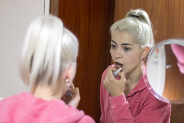 美丽的年轻女子在浴室对着镜子化妆。图片下载